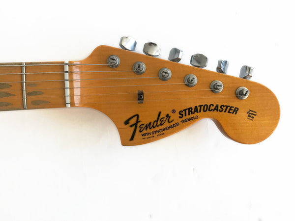 Close-up of Fender Stratocaster electric guitar headstock with tuning pegs and logo on natural wood finish