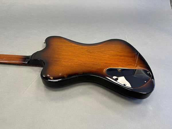 Electric guitar back view with sunburst finish and black plastic control cavity cover on gray background