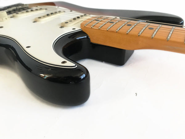 Close-up of black electric guitar body and maple neck with white pickguard on white background