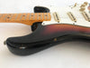 Close-up of sunburst electric guitar body with maple neck and white pickguard showing wear and chip marks on the finish