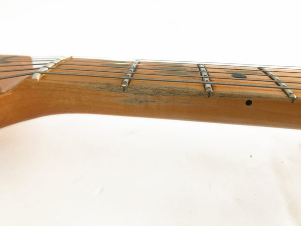 Close-up of worn maple guitar neck with metal frets and black dot inlays on light background