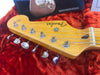 Close-up of Fender Stratocaster guitar headstock with six tuning pegs and strings on red plush background