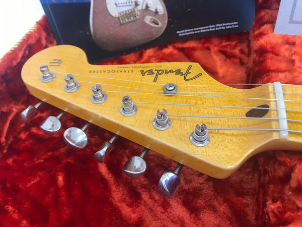 Close-up of Fender Stratocaster guitar headstock with six tuning pegs and strings on red plush background