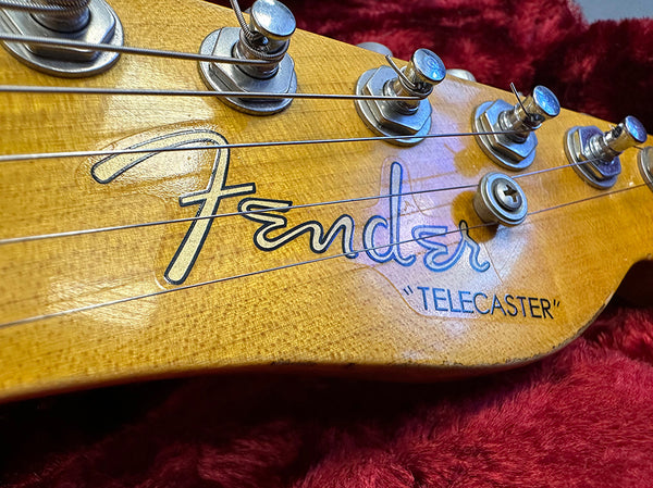 Close-up of Fender Telecaster guitar headstock with tuning pegs and strings on a red plush background