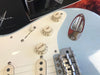 Close-up of light blue electric guitar body showing white tone and volume control knobs, chrome bridge, and jack plate