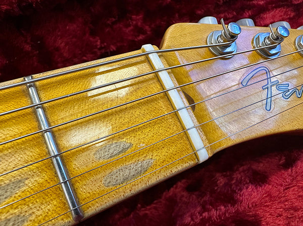 Close-up of Fender electric guitar headstock and worn maple fretboard with metal frets and tuning pegs on red plush background