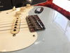 Close-up of electric guitar bridge, strings, volume and tone knobs on cream pickguard with light blue body and vintage wear finish