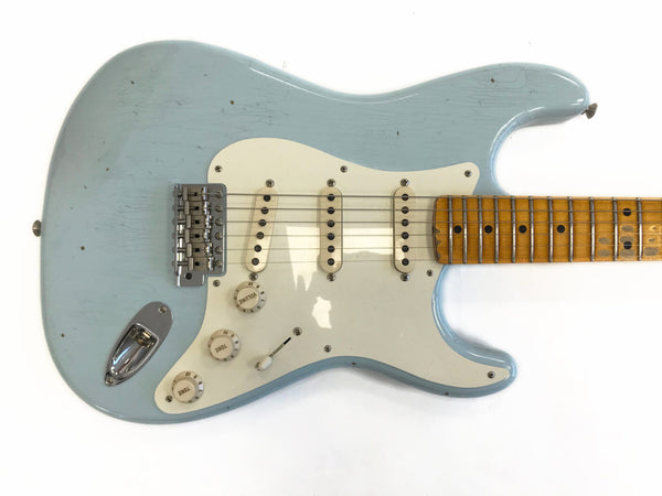Vintage light blue electric guitar with maple fretboard and white pickguard, showing worn finish and three single-coil pickups.