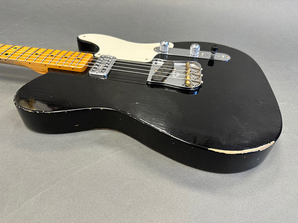 Black electric guitar with maple neck and white pickguard, showing minor wear and scratches on body edges, close-up view
