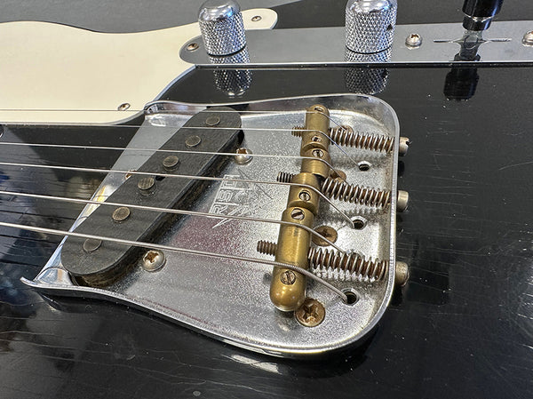 Close-up of vintage electric guitar bridge, pickup, and control knobs on black body with cream pickguard