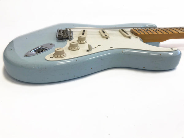 Light blue electric guitar with white pickguard and three single-coil pickups, vintage style tone and volume controls, maple fretboard, and chrome bridge hardware on white background
