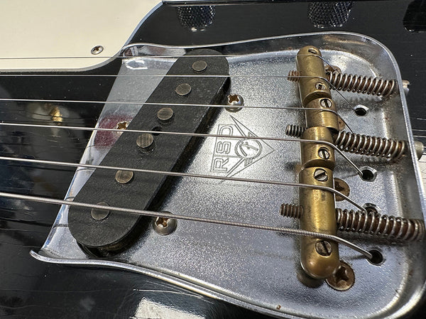 Close-up of vintage Fender RS-7 guitar bridge and single-coil pickup with strings and springs on black electric guitar body
