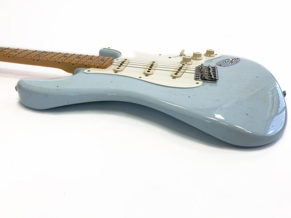 Light blue electric guitar with white pickguard and maple neck, vintage style with single-coil pickups and tremolo bridge, shown on white background
