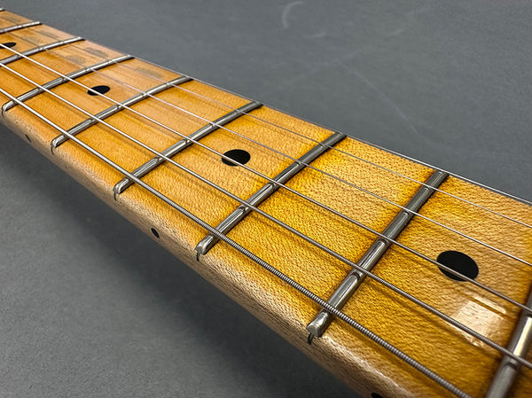 Close-up of maple guitar fretboard with metal frets and steel strings on gray background