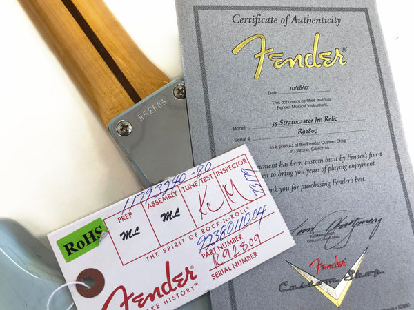 Close-up of Fender 55 Stratocaster Jm Relic guitar neck with serial number R92809 and authentic Fender Custom Shop certificate of authenticity dated 10/18/17 alongside Fender inspection and assembly tag with RoHS compliance label.