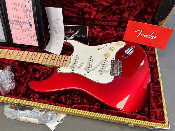 Red Fender Stratocaster electric guitar with maple neck and white pickguard in a plush red velvet-lined hardshell case with Fender owner's manual and paperwork