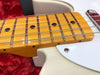 Close-up of maple fretboard and strings on white electric guitar with black dot inlays and chrome screw on pickguard against red fabric background