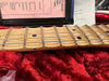 Close-up of maple guitar neck and fretboard with metal frets and black dot inlays resting on red plush fabric, with guitar setup and adjustment documents in the background.