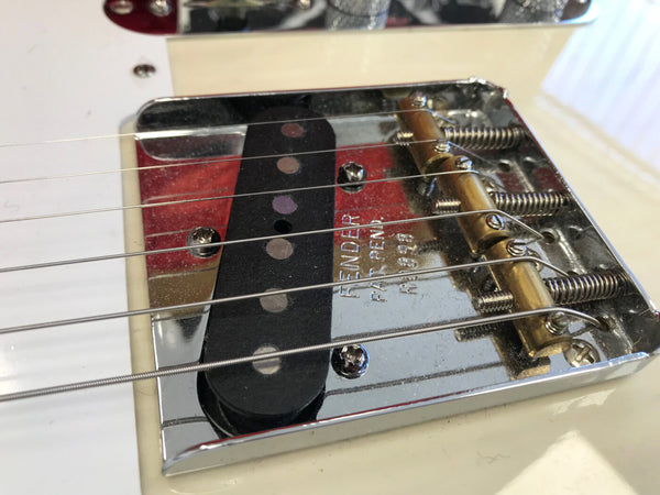 Close-up of Fender Telecaster guitar bridge and single-coil pickup with strings and brass saddles on white body electric guitar