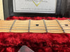 Close-up of maple guitar neck and frets inside red plush-lined Fender Custom Shop guitar case with Custom Shop certificate visible in background