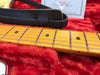 Close-up of maple neck and fretboard with dot inlays on Fender electric guitar resting on plush red guitar case lining with black leather strap visible