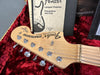 Close-up of Fender Stratocaster guitar headstock with chrome tuning pegs and included Fender Lacquer Finishes care manual in red plush-lined guitar case