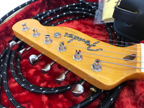 Close-up of Fender Telecaster maple guitar headstock with chrome tuning pegs and black braided guitar cable on red plush case lining