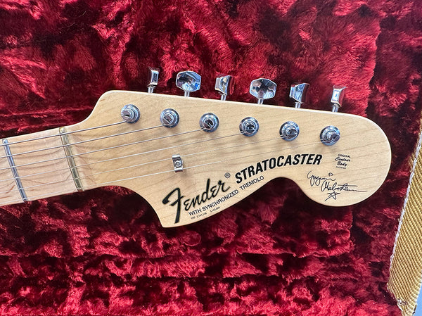 Close-up of Fender Stratocaster guitar headstock with chrome tuning pegs and maple wood finish on red velvet background