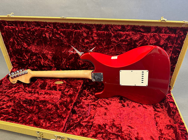 Red electric guitar with maple neck inside vintage-style gold and red velvet lined hard case, rear view showing neck plate and tremolo cavity cover.