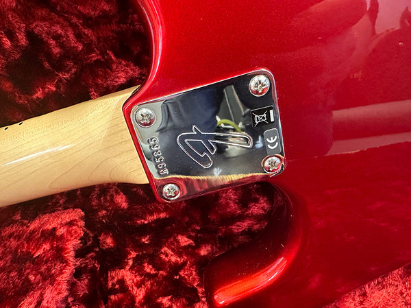 Close-up of red electric guitar neck plate with serial number R953863 and Fender logo, resting on red plush fabric.