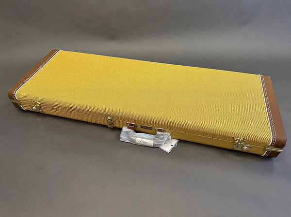 Closed yellow tweed guitar case with brown leather corners and a wrapped handle on gray background