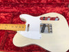 Close-up of white solid body electric guitar with maple neck and black dot inlays resting in red velvet-lined guitar case