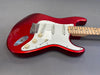 Red electric guitar with white pickguard, maple neck, and three single-coil pickups on gray background