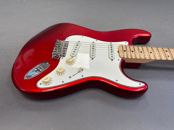 Red electric guitar with white pickguard, maple neck, and three single-coil pickups on gray background