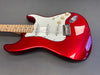 Red electric guitar with maple neck and white pickguard, three single-coil pickups, and chrome hardware on gray surface
