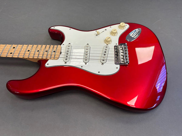Red electric guitar with maple neck and white pickguard, three single-coil pickups, and chrome hardware on gray surface