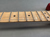 Close-up of maple guitar neck and fretboard with metal frets and black dot inlays on gray background