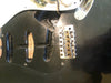 Close-up of black Fender Stratocaster electric guitar body showing empty pickup cavities, serial number stamp inside cavity, and vintage-style bridge with six adjustable saddles and "Fender" engravings on saddles