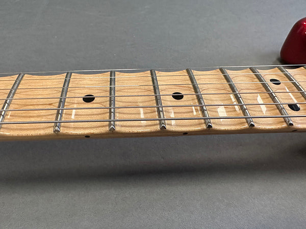 Close-up of maple guitar neck and fretboard with metal frets and black dot inlays on gray background