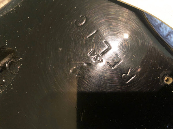 Close-up of serial number etched on black electric guitar body with visible wear and scratches, showing authenticity detail for guitar identification.