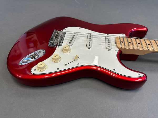 Red electric guitar body with white pickguard and maple neck, featuring three single-coil pickups and chrome hardware on gray background