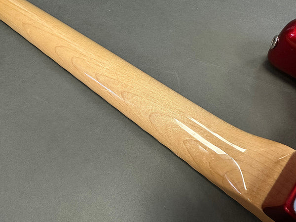 Close-up of glossy maple neck of electric guitar with red body corner visible on grey surface