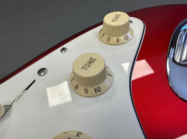 Close-up of cream tone control knobs on red electric guitar with white pickguard and chrome hardware