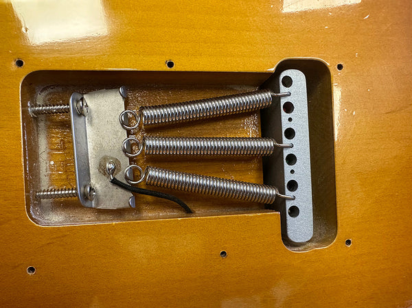 Close-up of electric guitar tremolo spring cavity with three metal springs and mounting hardware on natural wood finish body