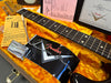 Close-up of Fender Custom Shop tremolo system and rosewood fretboard on guitar neck inside orange plush-lined guitar case with Fender Custom Shop paperwork and parts, showcasing vintage style guitar components.