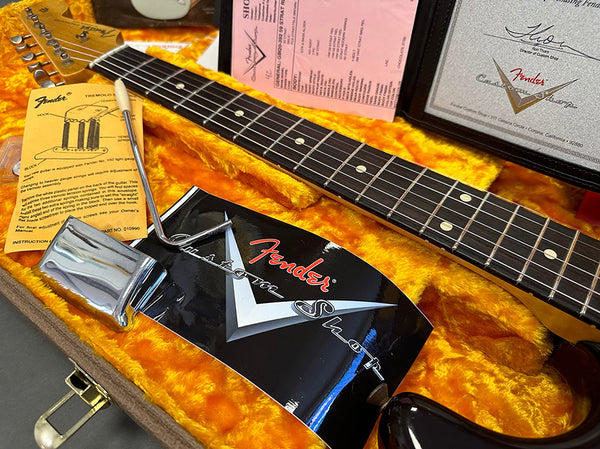 Close-up of Fender Custom Shop tremolo system and rosewood fretboard on guitar neck inside orange plush-lined guitar case with Fender Custom Shop paperwork and parts, showcasing vintage style guitar components.