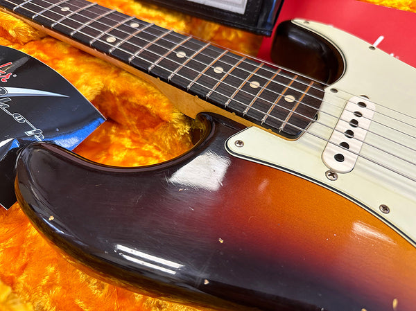 Close-up of vintage sunburst electric guitar body and fretboard with white pickups and pickguard on orange plush guitar case interior