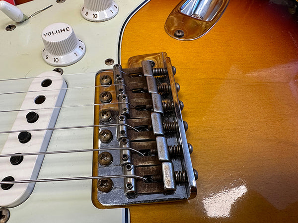 Close-up of electric guitar bridge and strings on sunburst body with white volume knob and pickups