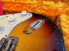 Close-up of vintage sunburst electric guitar body with tone control knobs and chrome input jack plate on orange plush guitar case lining