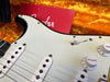 Close-up of white Fender Stratocaster electric guitar pickups and volume knob inside orange plush-lined guitar case with red Fender booklet
